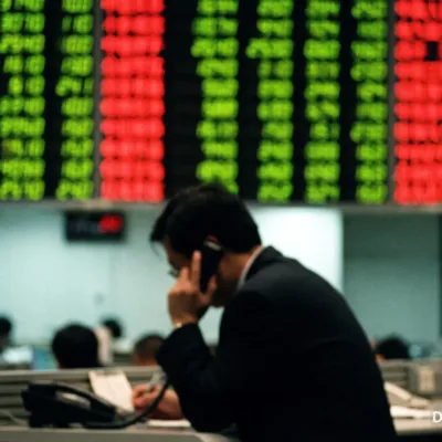 Trader on the phone in front of a stock market display board